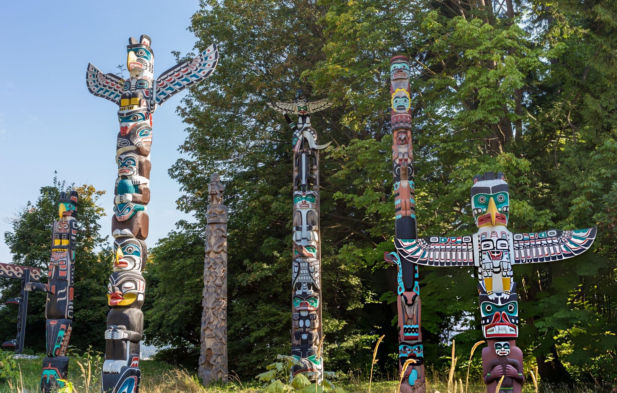 Indigenous totem poles surrounded by trees in Stanley Park Vancouver, showcasing traditional carved figures and natural forest setting